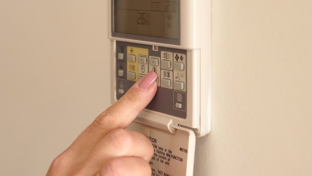 On-wall air conditioner remote control, adjust temperature in room. Press start to turn on - hand adjusting a wall mounted thermostat temperature for the room air conditioning system.