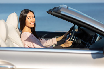 portrait of smiling asian girl sitting in cabriolet and looking at the camera