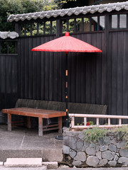 Red paper parasol and wooden bench against black wooden wall with roof tiles in a Japanese tea garden