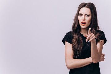 Beautiful surprised woman making a blaming index finger gesture at camera isolated light background copyspace