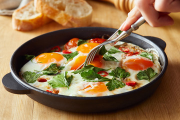 cropped view of eating fried eggs with parsley and chili pepper on wooden table with fork and knife