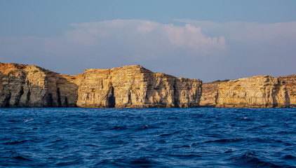 Rocky edges of the Comino island sticking out from Mediterranean Sea and lit by the orange evening sun. Rock formations with caves.