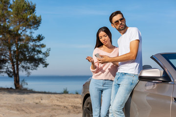 woman and man standing at the car and using at smartphone