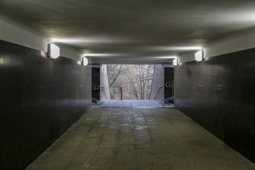 An empty underpass to a city park with light at the end.