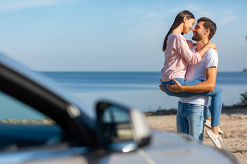 asian woman in love looking at her boyfriend holding her on the hands with car in foreground