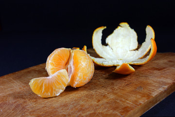 Pieces of mandarin in front of the remaining peel close up with black background