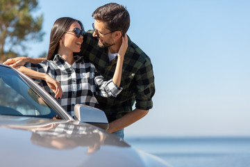 portrait of couple in sunglasses standing at the car and embracing together