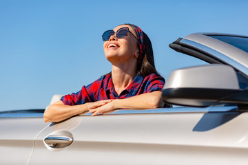 cheerful asian woman in sunglasses sitting in convertible smiling and looking up