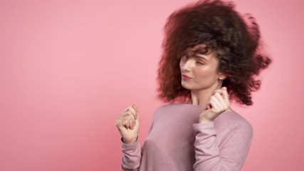 Beautiful woman with curly hair dancing with head on pink studio background. Cute girls portrait. Party, happiness, freedom, youth concept.