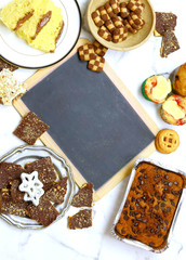 Flat lay image of a variety of baked sweet breads and cookies on a marble surface with a chalkboard in the center for your message.