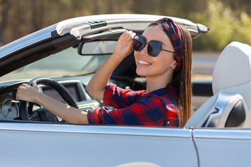 woman wearing sunglasses sitting in convertible and smiling at the camera