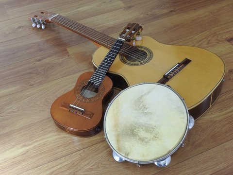 An acoustic guitar and two Brazilian musical instruments: cavaquinho and pandeiro (tambourine), on a wooden surface. The instruments are widely used to accompany samba and choro, Brazilian rhythms.