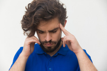 Closeup of focused tired guy touching head, thinking hard or suffering from headache. Handsome bearded young man in blue casual t-shirt posing isolated over white background. Concentration concept