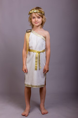 Cute child dressed like ancient roman god. Mascarade costume for holidays. Studio shot gray...