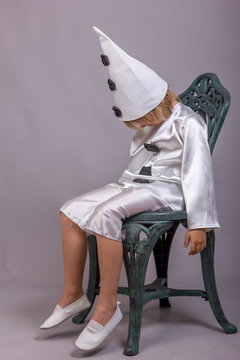 Cute child dressed like Pierrot, sad clown. Mascarade costume for holidays. Studio shot on gray background. Emotional concept.
