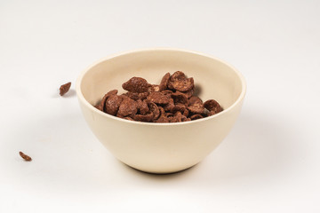 Chocolate corn flakes falling to the white bowl isolated on white. Motion.