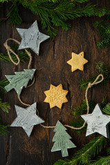 New Year garland from ginger cookies and little craft wooden stars and firs on brown wooden background. Christmas decoration in Scandinavian style