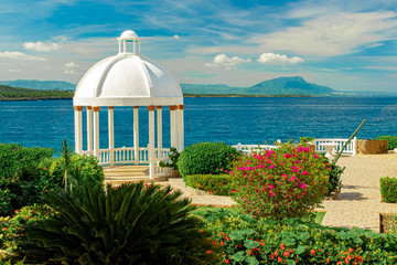 Beautiful white gazebo and tropical flower garden on Caribbean ocean background, summer mountain...