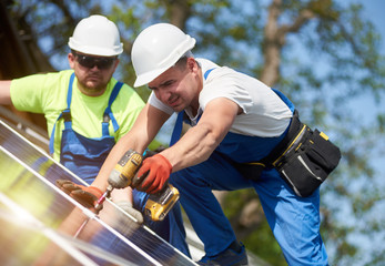 Two professional technicians connecting solar photo voltaic panel to metal platform using screwdriver. Stand-alone solar system installation, alternative renewable energy generation concept. © anatoliy_gleb