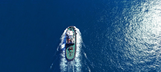 Aerial drone ultra wide photo of industrial tug assisting boat ass in deep blue Mediterranean sea