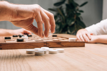 Side view of man holding white checkers while playing with woman at table