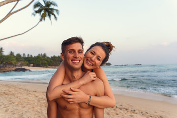young happy couple piggyback in a tropical beach during sunset