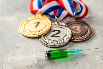 Doping for athletes. Golds, silver and bronze medal and doping syringe on a gray background