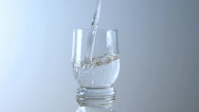 Pouring clear water into a drinking glass, gray background with copy space