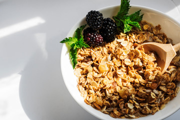 Blackberry with mint leaves, in a plate with granola with milk, on a white background with hard shadows. Selective focus. Copy space