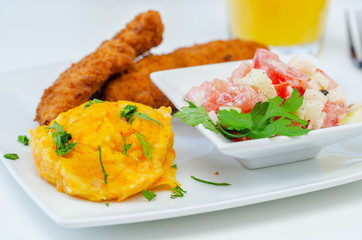 Breaded and herbed chicken breast fillet served with mashed carrots with potatoes  and  tomato salad with onions