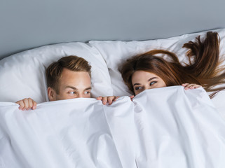Playfull couple peeping from bedsheet