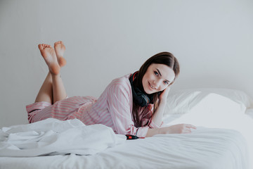 woman in pajamas listening to music with headphones on the bed