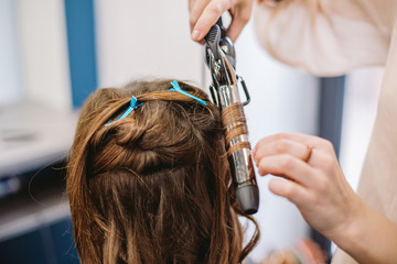 beauty, hairstyle concept, happy young woman and hairdresser with hair iron making hairdo at hair...