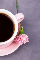 Pink cup of black coffee and pink carnation flower on a gray concrete background