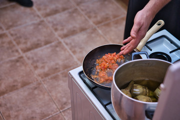 Cooking a homemade tomato sauce in a frying pan on a gas fire and simmering artichokes with oil and charcoal. Hand of adult man.