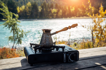 Copper turk with coffee on gas burner on the background of river and hills. Coffee preparing on the...