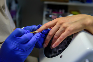 Cuticle removal, close-up. Manicure in the salon. Manicurist in blue gloves shifts the cuticle of the nail with metal spatula.