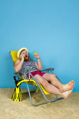 Happy young man resting, takes selfie, drinking cocktails on blue studio background. Concept of human emotions, facial expression, summer holidays or weekend. Chill, summertime, sea, ocean, alcohol.