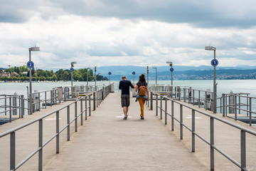 Loving couple walking at cruise ship dock at the Lake of Zurich with background of buldings at the lakeshore in Zurich, Switzerland.