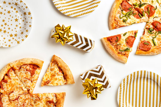 Birthday with junk food. Two large tasty pizzas with pepperoni and cheese on a white plate. Gifts on the holiday table. Top view with copy space for text. Flat lay