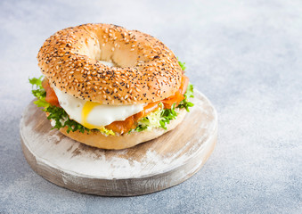 Fresh healthy bagel sandwich with salmon, ricotta and soft egg on vintage chopping board on white...