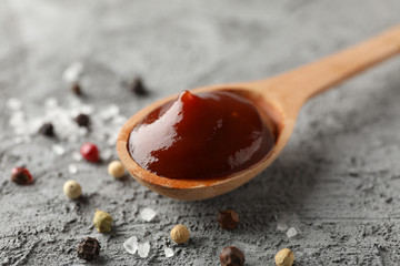 Spoon of delicious barbeque sauce, ingredients on grey background, space for text. Closeup