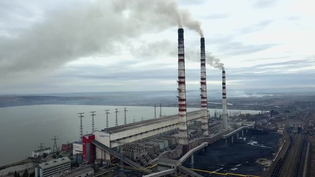 Aerial view of high chimney pipes with grey smoke from coal power plant. Production of electricity with fossil fuel.