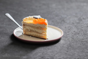 Cake with cottage cheese filling, jelly, fruit, sprinkled with coconut shavings on a dark gray background