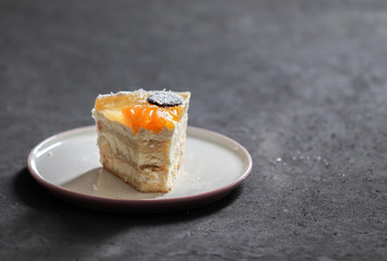 Cake with cottage cheese filling, jelly, fruit, sprinkled with coconut shavings on a dark gray background