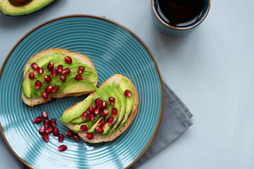 Avocado sandwich on bread made with fresh sliced avocados and pomegranate seeds on gray wooden background. Top view. Healthy eating concept. Copy space
