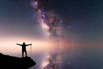 Beautiful starry night, hikers silhouette stands on  the rock and looks at the Milky Way galaxy.