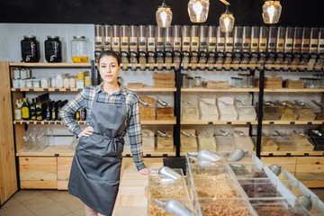 Young Mixed Race Woman Owner Selling Superfoods in Zero Waste Shop. Lots of Healthy Food in Glass...