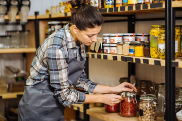 Concept of zero waste shop. Woman holding large glass jar with groceries on interior background of...