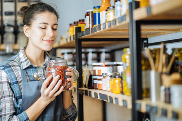 Concept of zero waste shop. Woman holding large glass jar with groceries on interior background of...